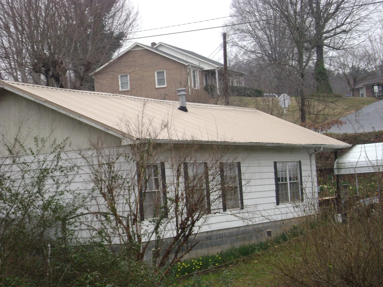 Tan metal roof on a white sided house set into a hillside — Commercial Roofing by Roofing Brothers in Durham