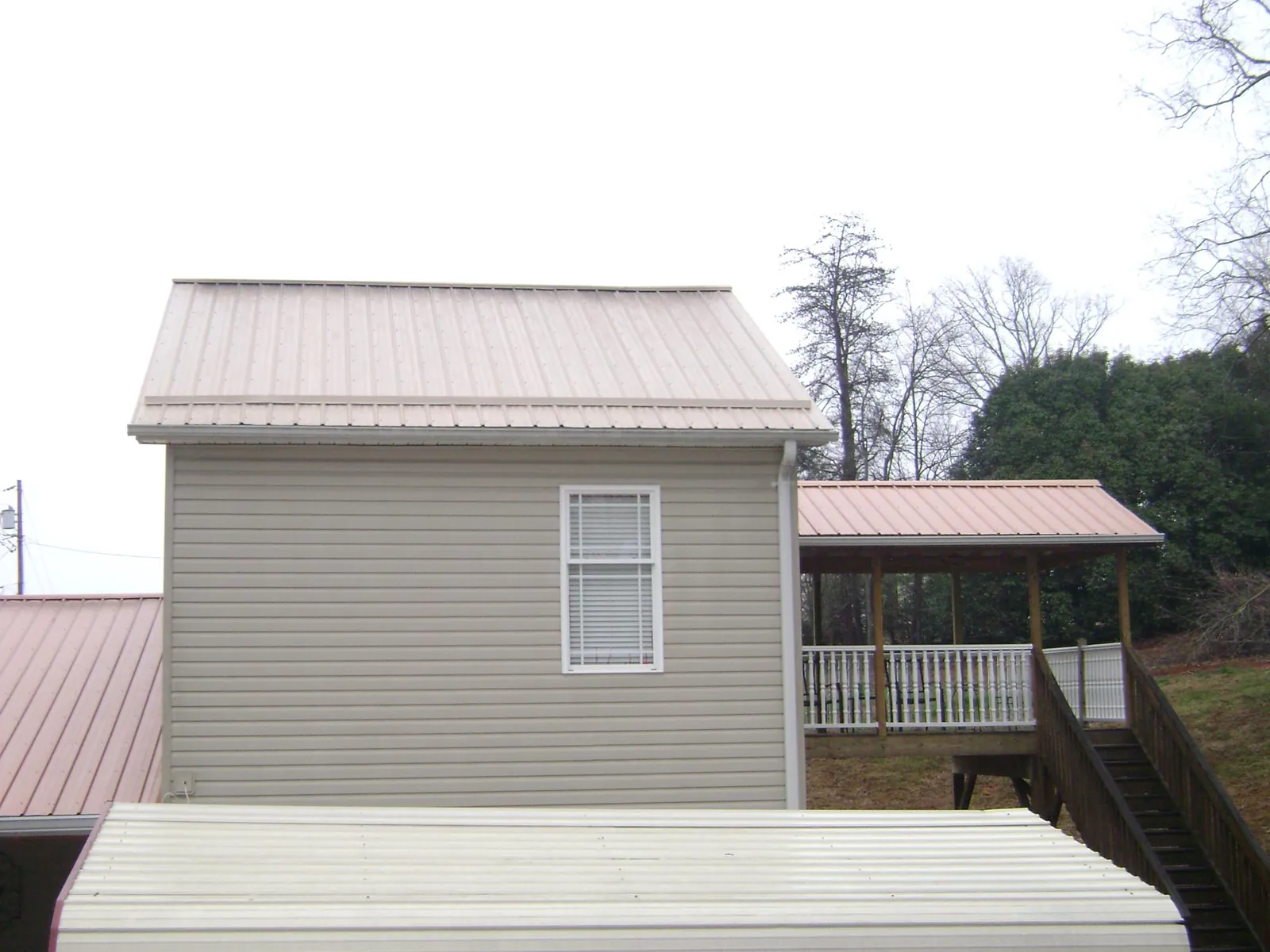 Tan metal roofs on a two story addition and attached porch, from a Roof Replacement job in Durham