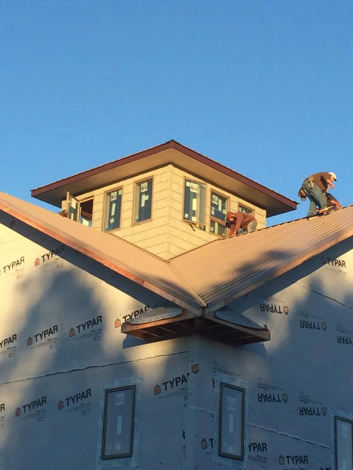 Roofers working around a rooftop cupola on a new metal roof at sunset — Roof Waterproofing in Durham by Roofing Brothers